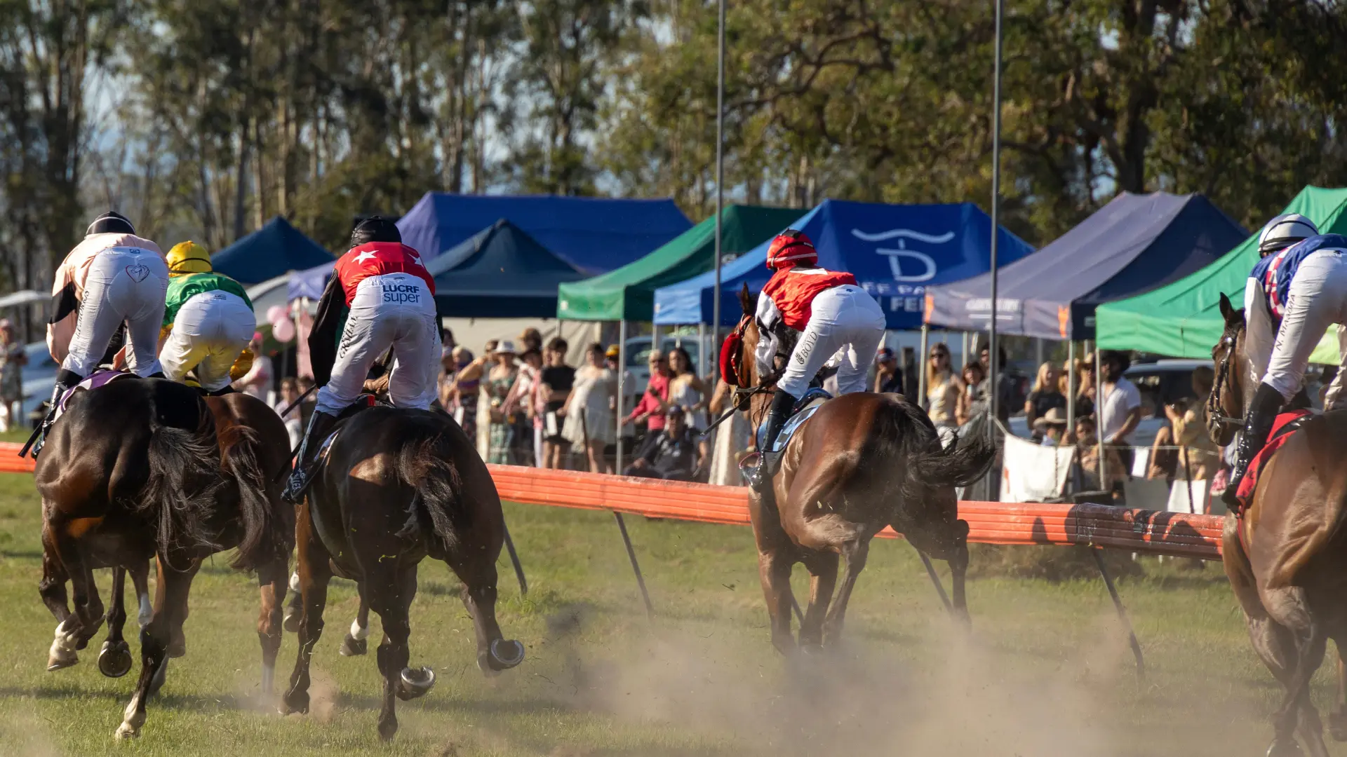 Horses and jockeys rounding the turn past the crowd at Tabulam Race Day, a country race meeting in Northern NSW